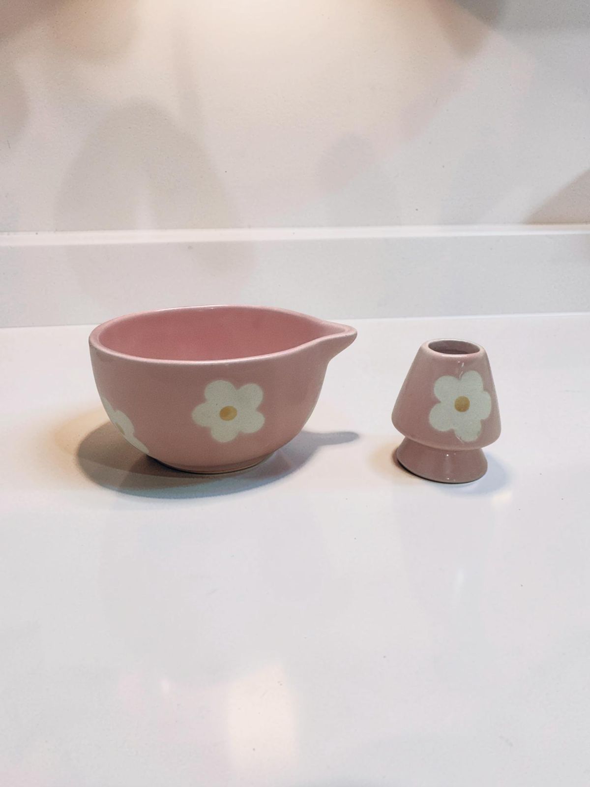 Aesthetic pastel pink matcha tea set featuring ceramic bowl, whisk holder, and traditional bamboo whisk on a minimalist table setup