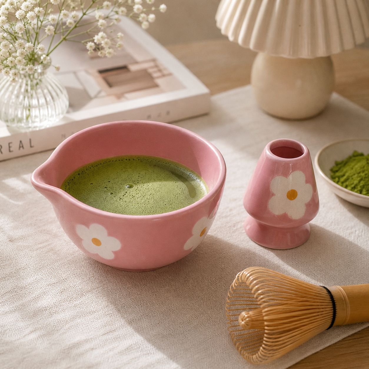 Pink ceramic matcha bowl with floral design and matching whisk holder on a cozy aesthetic tea setup