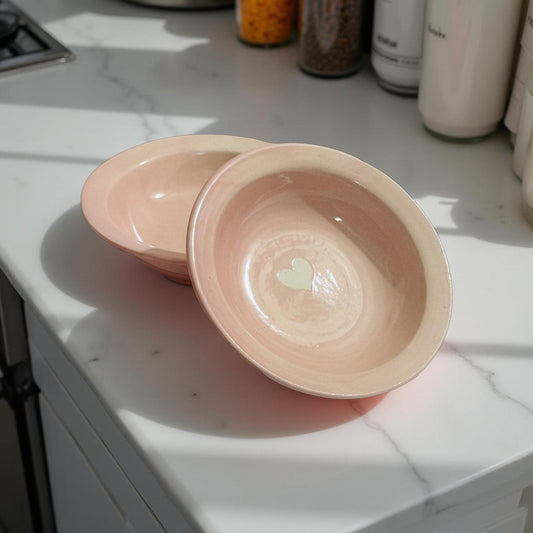 Blush pink ceramic bowls with heart design placed on a kitchen counter in sunlight
