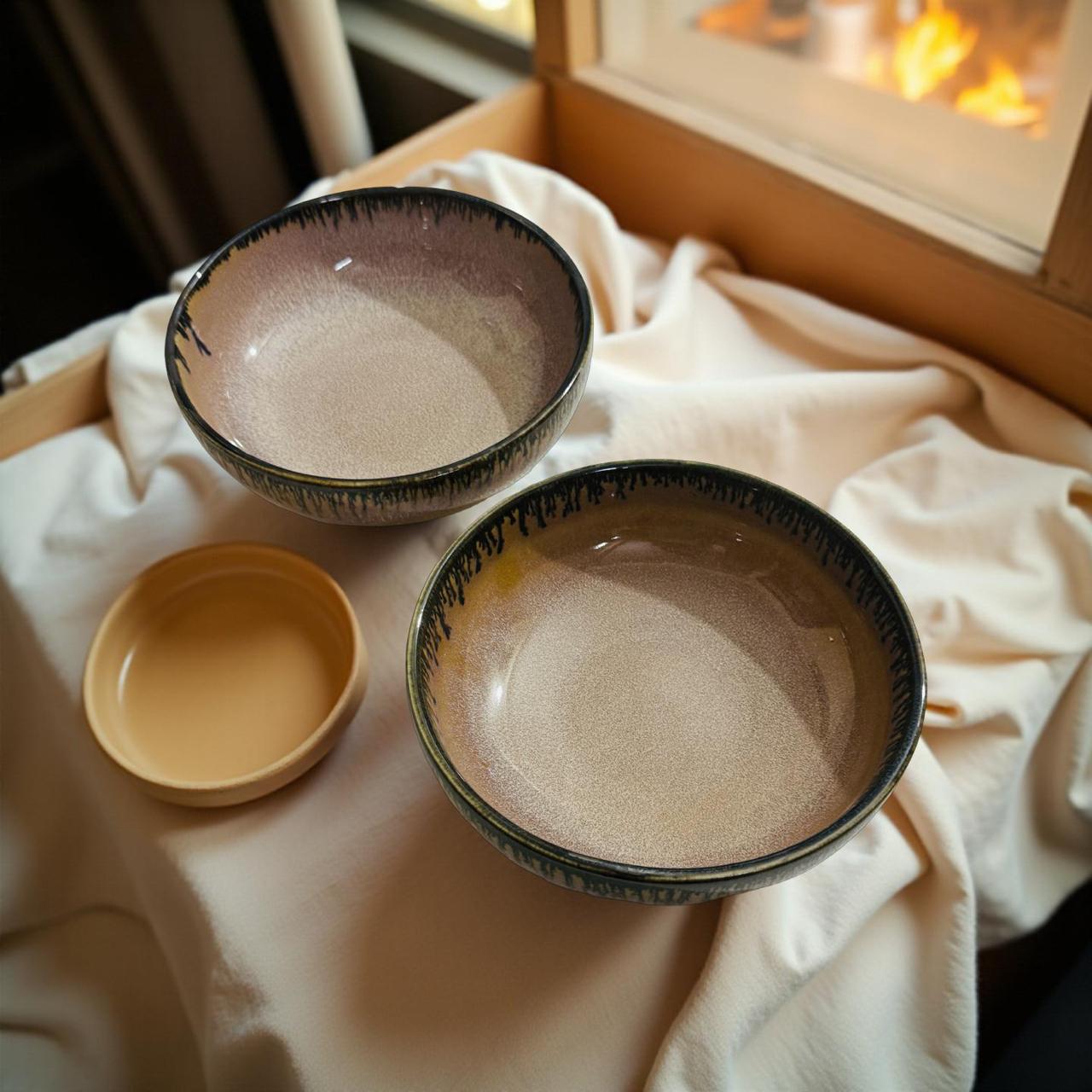 Three ceramic bowls on a light fabric with a fireplace in the background