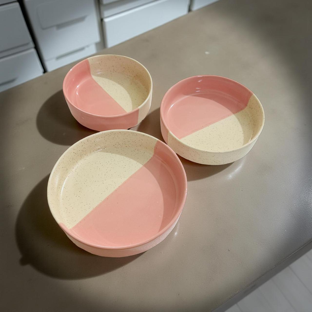 Three ceramic plates with pink and beige design on a kitchen counter.