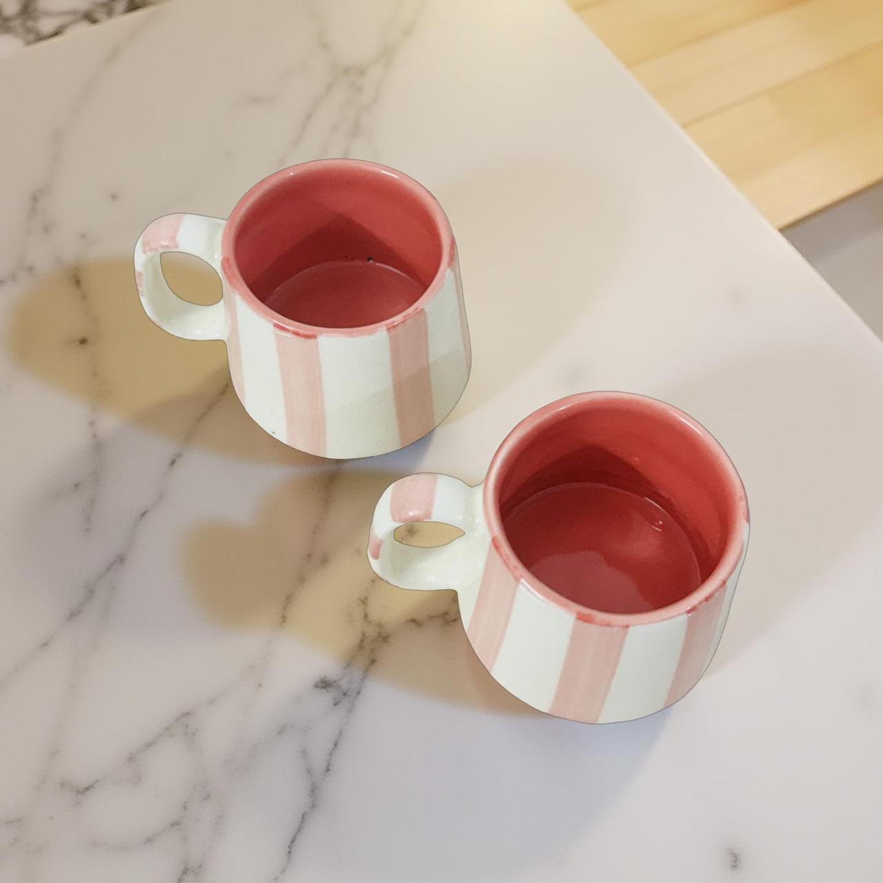 Two pink and white striped ceramic mugs on a marble surface.