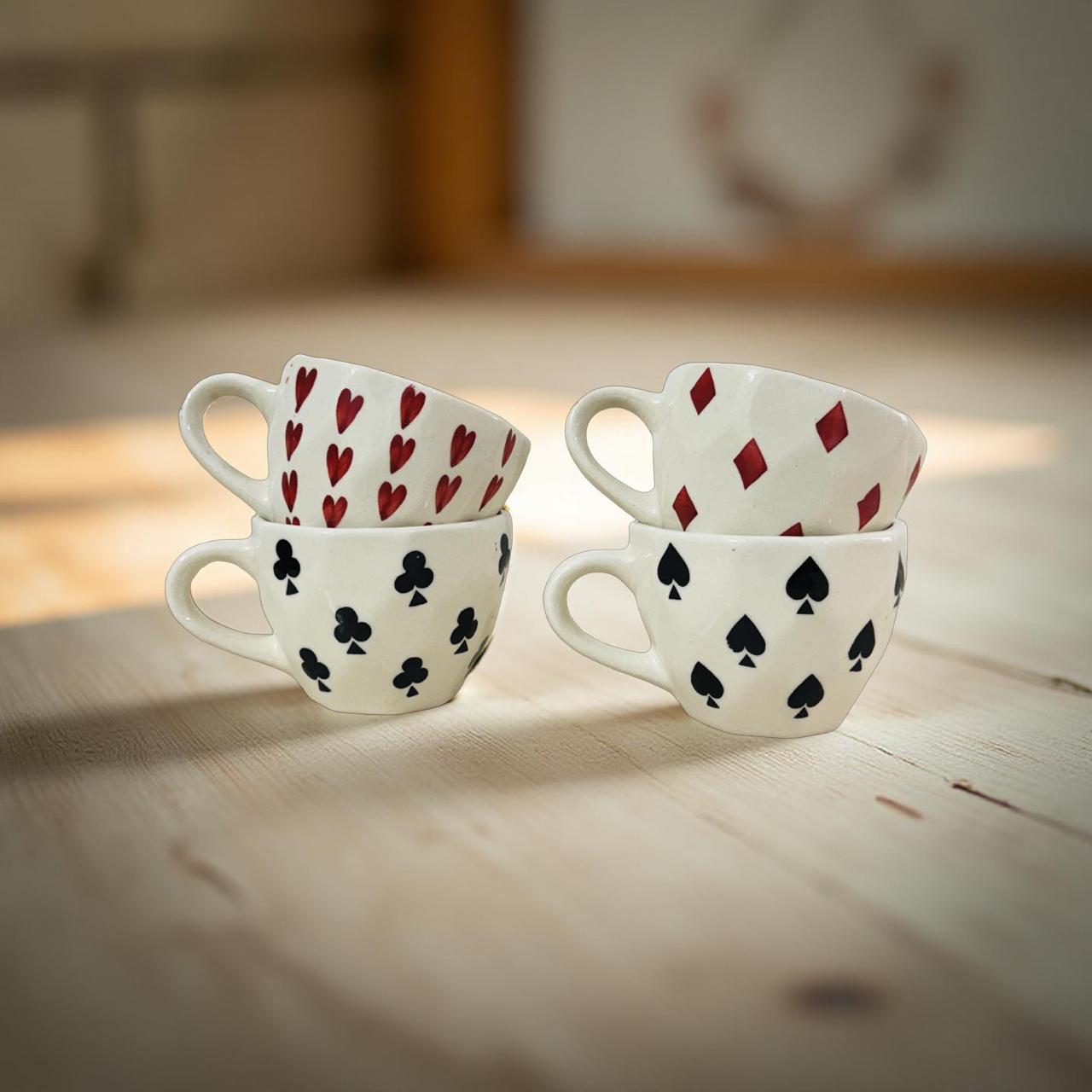 four ceramic coffee mugs in card theme pattern kept on a plain wooden surface 