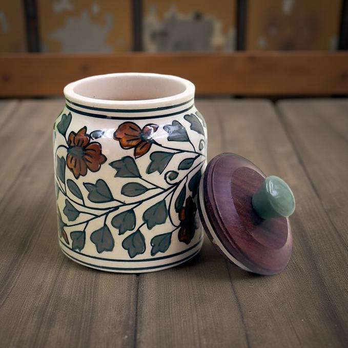 Ceramic jar with floral patterns and a wooden lid on a wooden surface