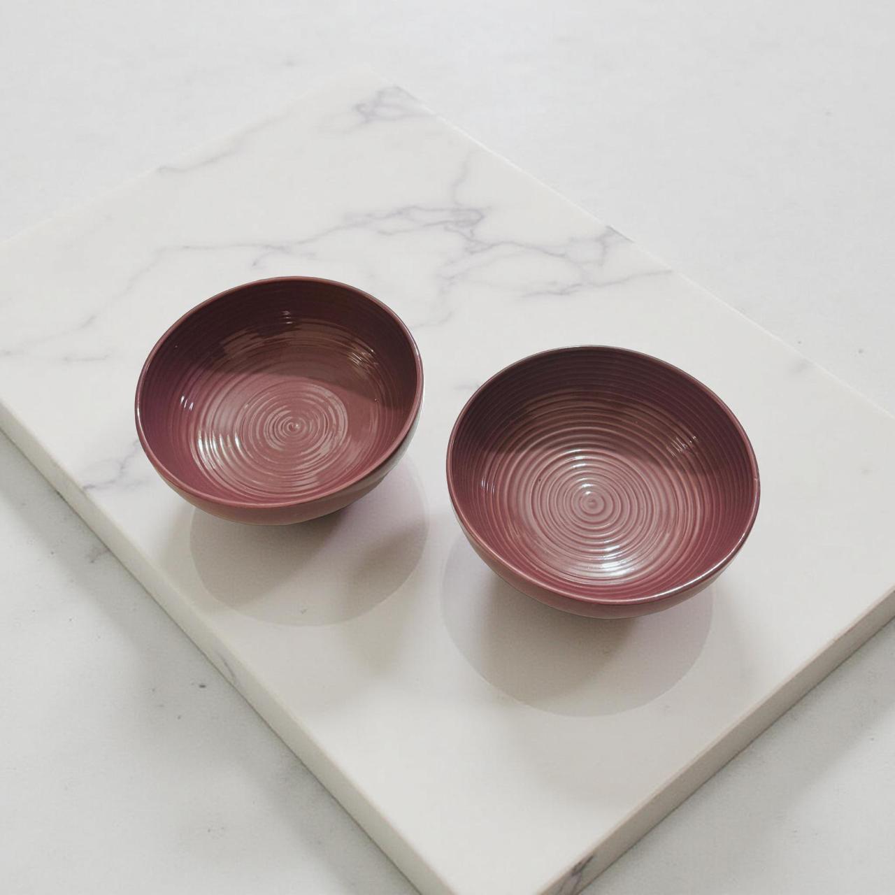 Two maroon ceramic bowls on a marble surface