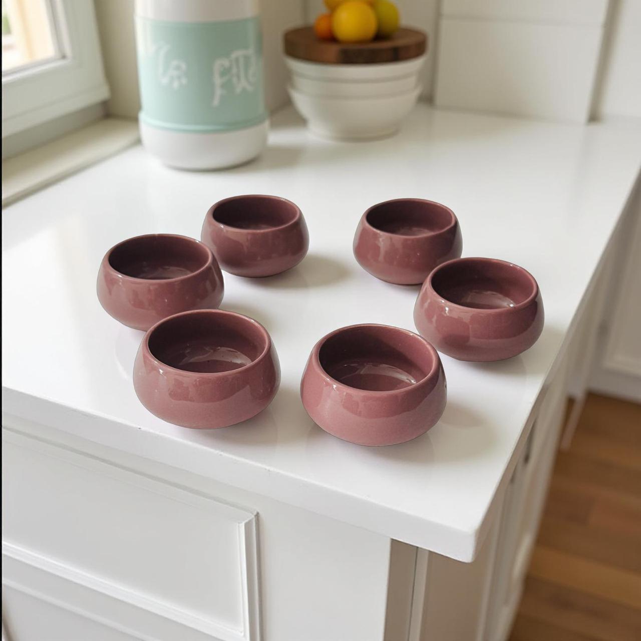 Set of six small pink ceramic bowls on a white surface with a blurred background