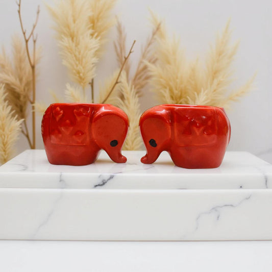 Two red elephant-shaped home decor accents on a marble surface with decorative plants in the background.