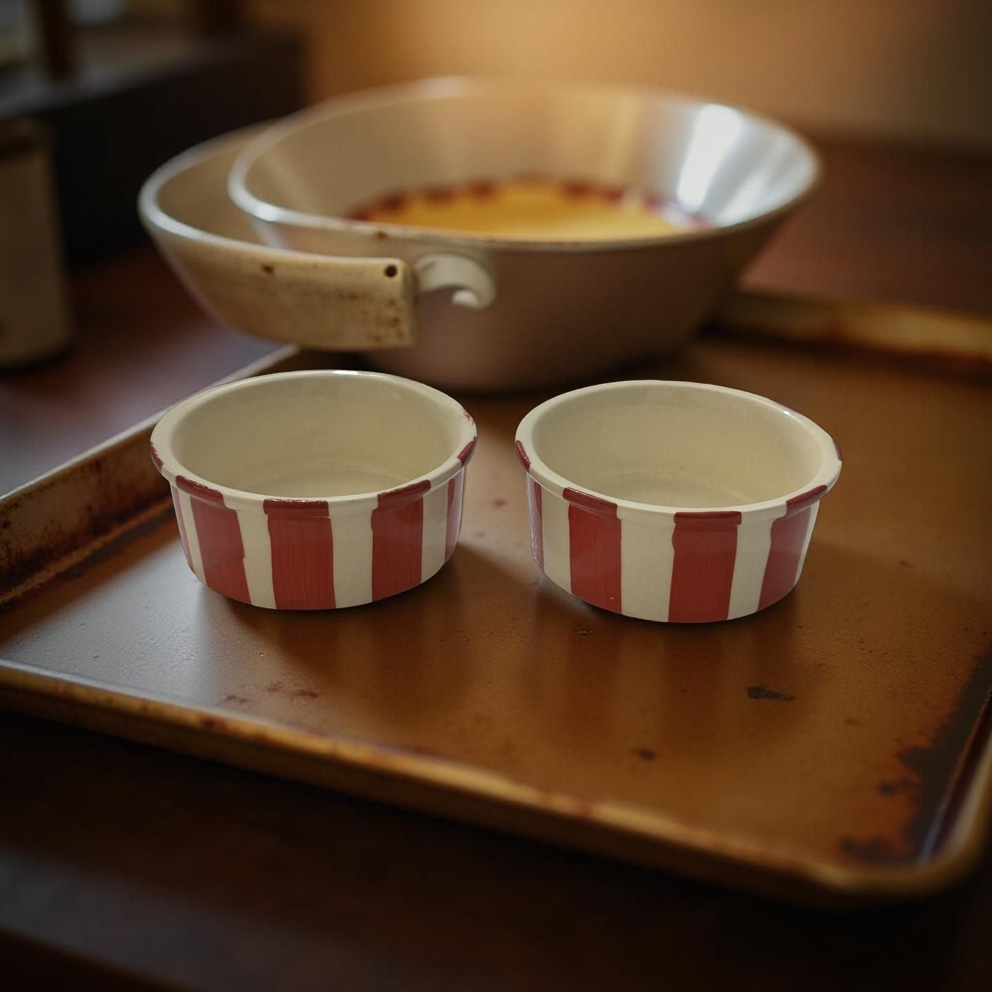 Two red and white striped ceramic ramekins on a metal tray with a blurred background.
