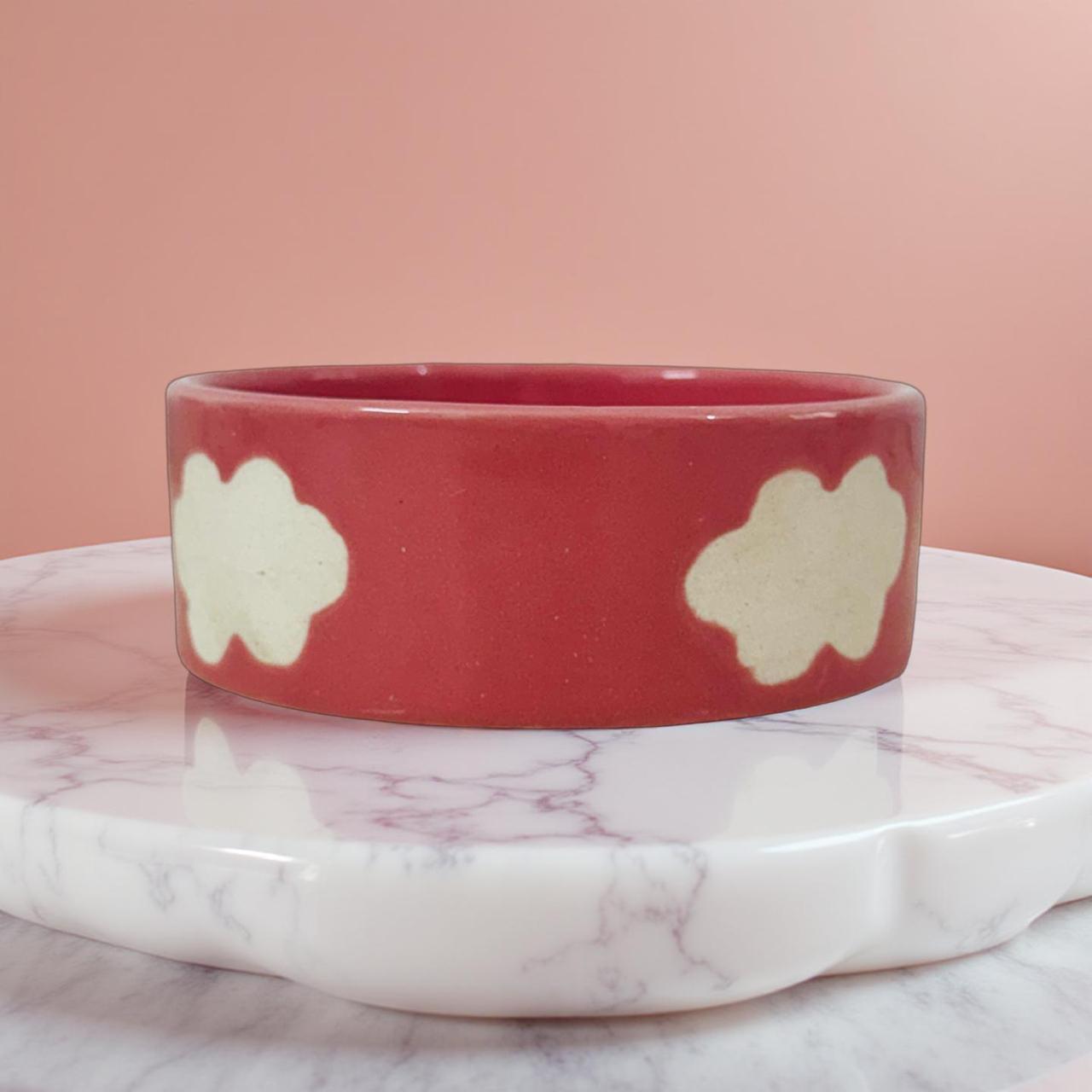 Red ceramic bowl with beige cloud patterns on a marble surface with pink background