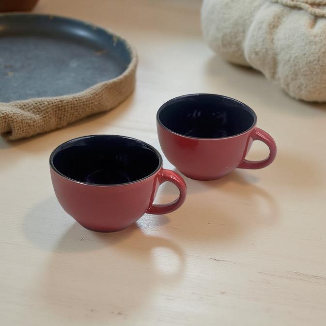 two red and black ceramic mugs placed on a natural wood finish kitchen platform 