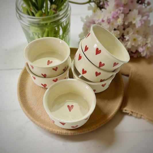 Set of small ceramic bowls with red heart patterns on a woven mat.