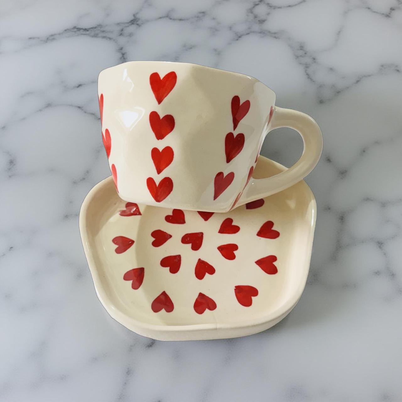 Ceramic cup and saucer set with red heart patterns on a marble background