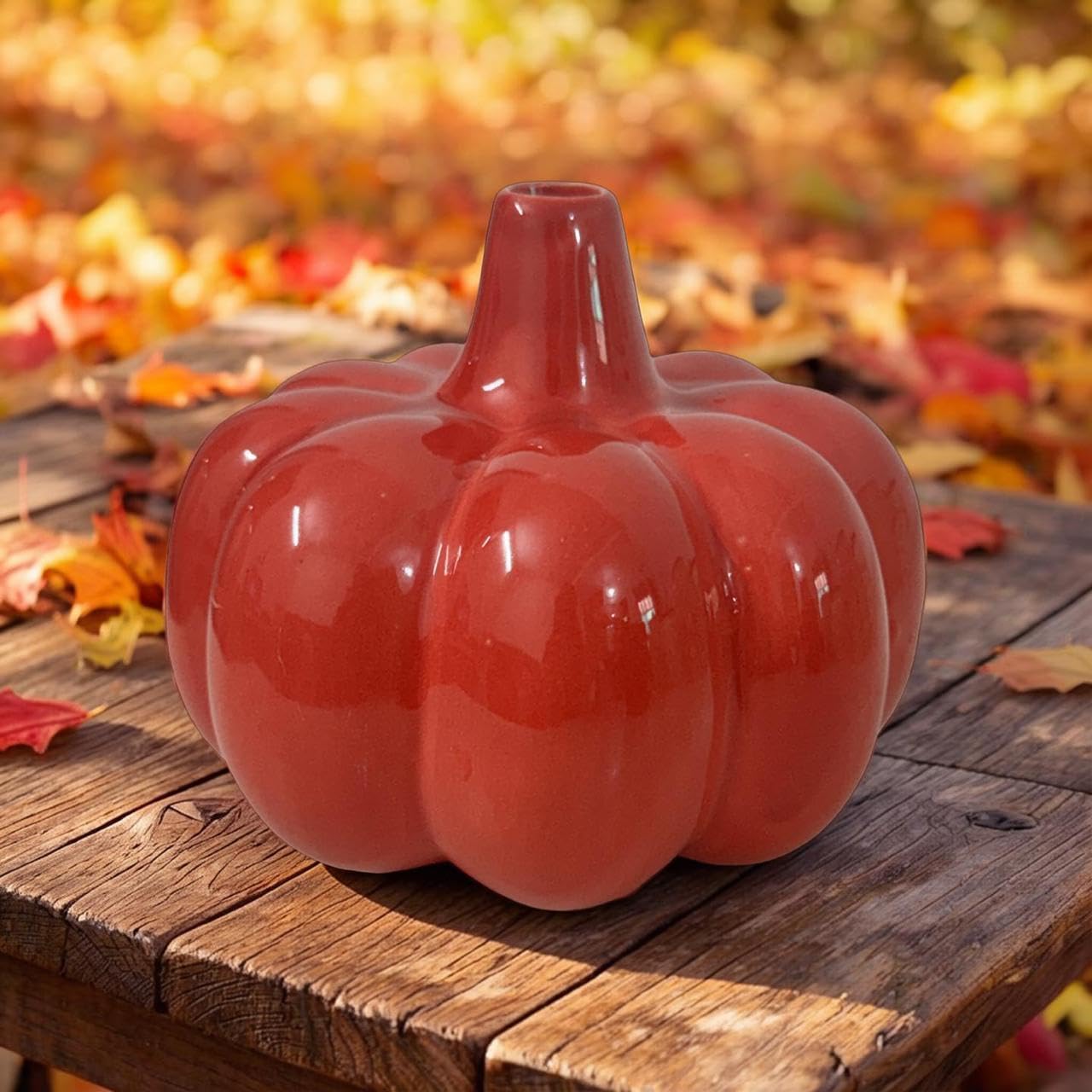 Red ceramic pumpkin on a wooden surface with blurred autumn leaves in the background