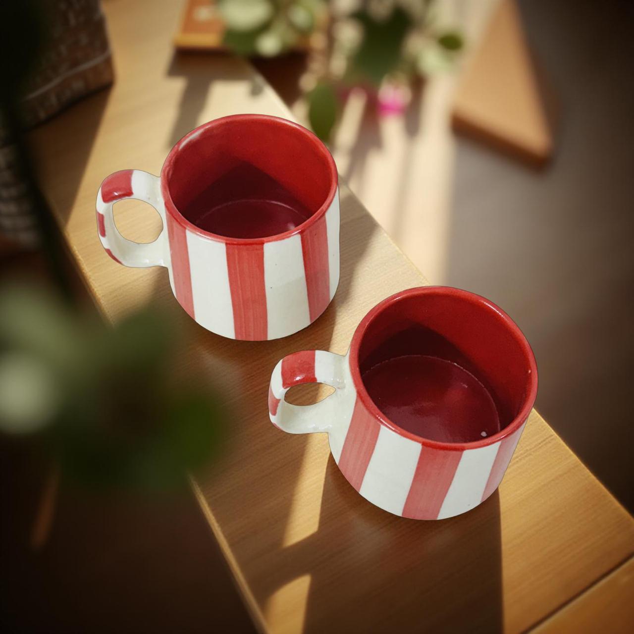 Two red and white striped mugs on a wooden surface with a blurred background