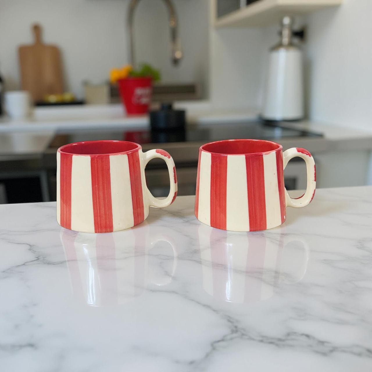 Two red and white striped mugs on a marble countertop with a kitchen background.