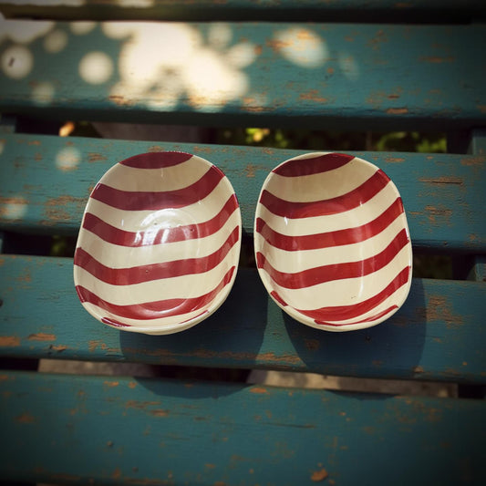 Two red and white striped ceramic bowls on a green metal bench.