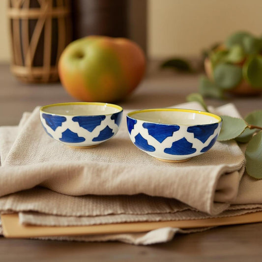 Two blue and white patterned bowls on a beige cloth with an apple and plant in the background.