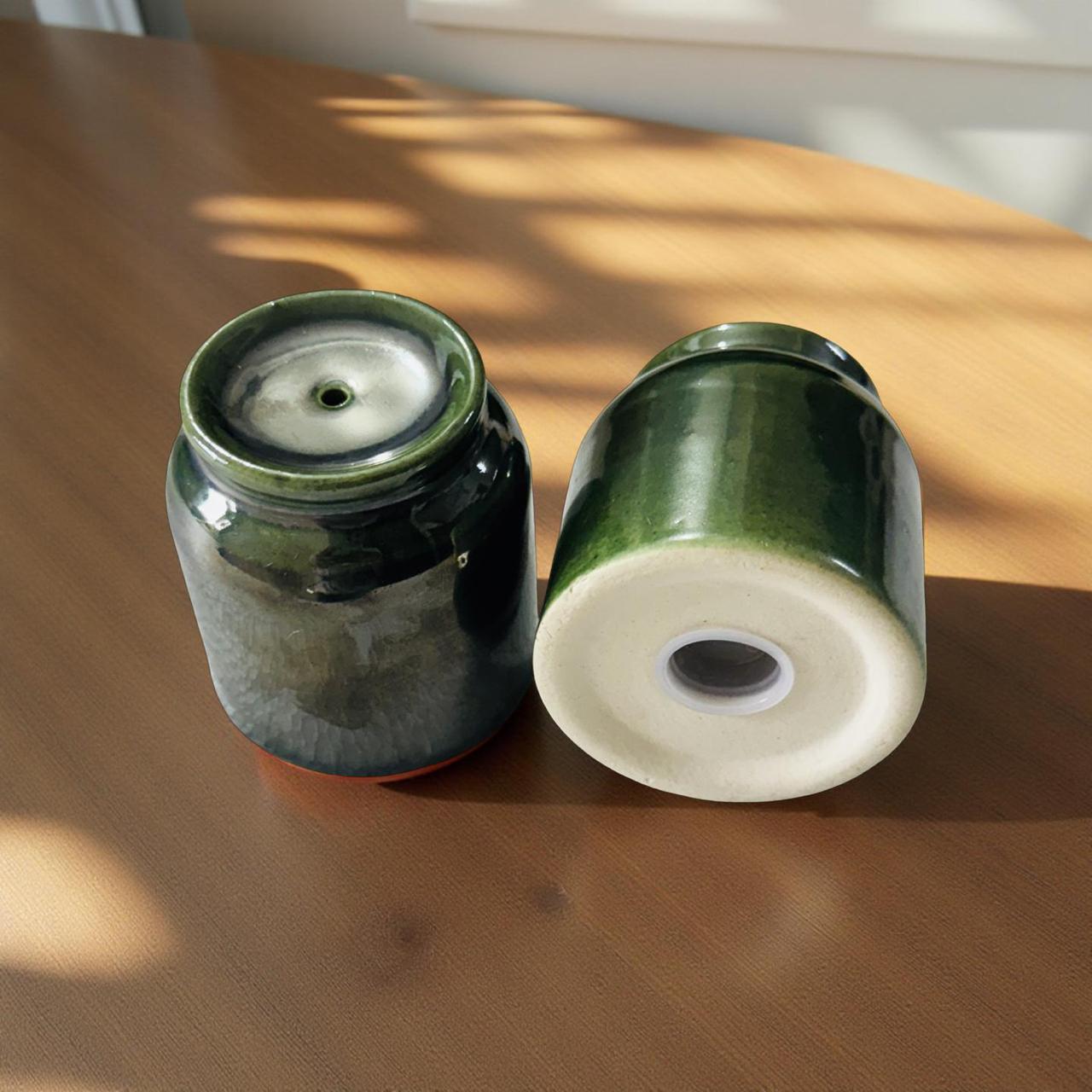 Two green ceramic jars on a wooden surface with sunlight casting shadows.