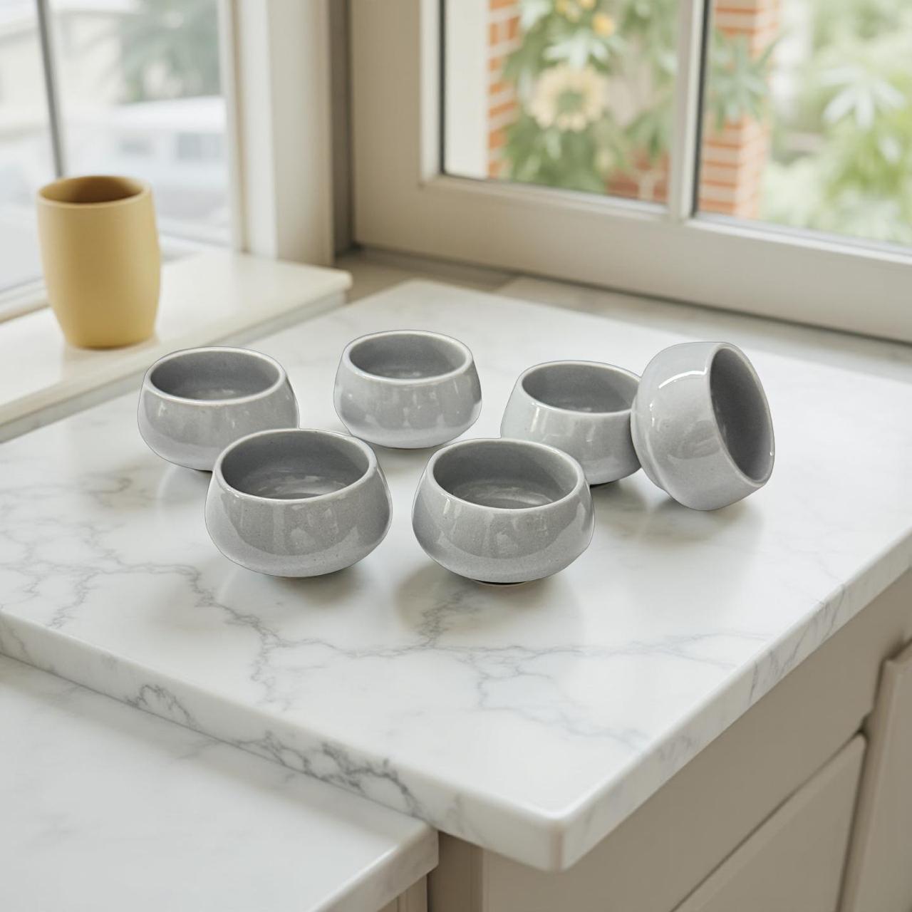 Set of six gray ceramic bowls on a marble countertop with a window in the background.