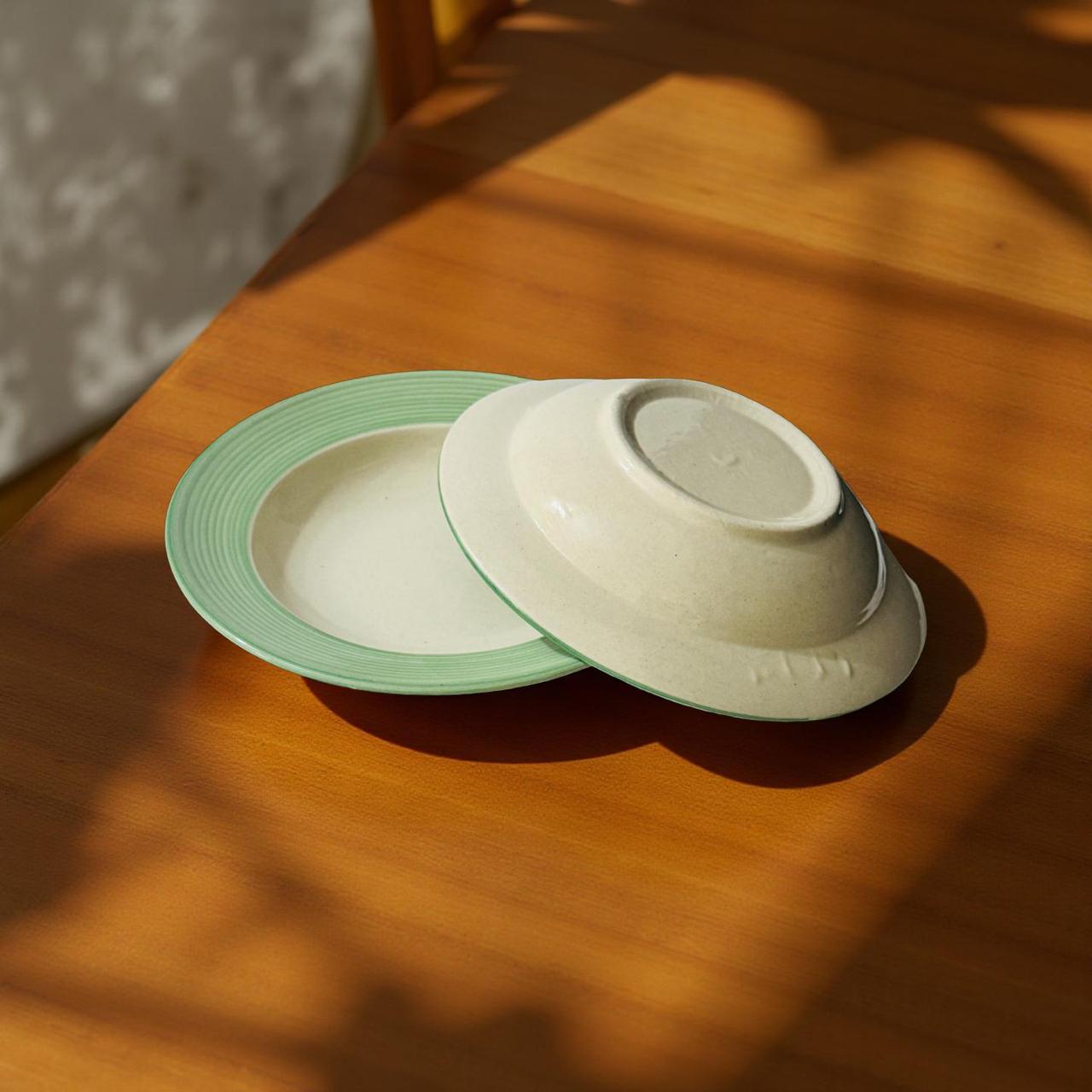 Two ceramic bowls, one green and one white, on a wooden surface with sunlight casting shadows.