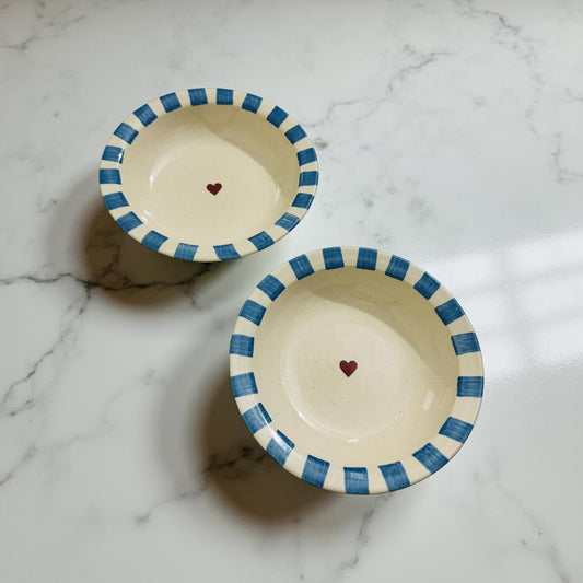 Two ceramic bowls with blue rims and red hearts on a marble surface