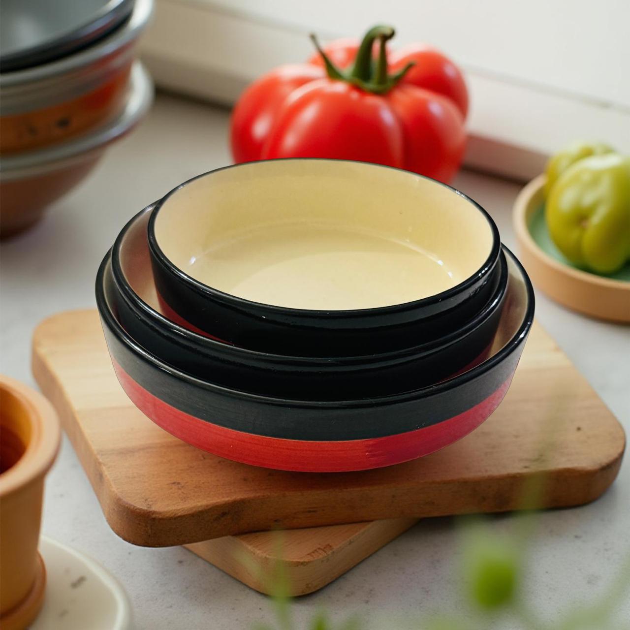 Set of ceramic bowls with red and black stripes on a wooden cutting board.