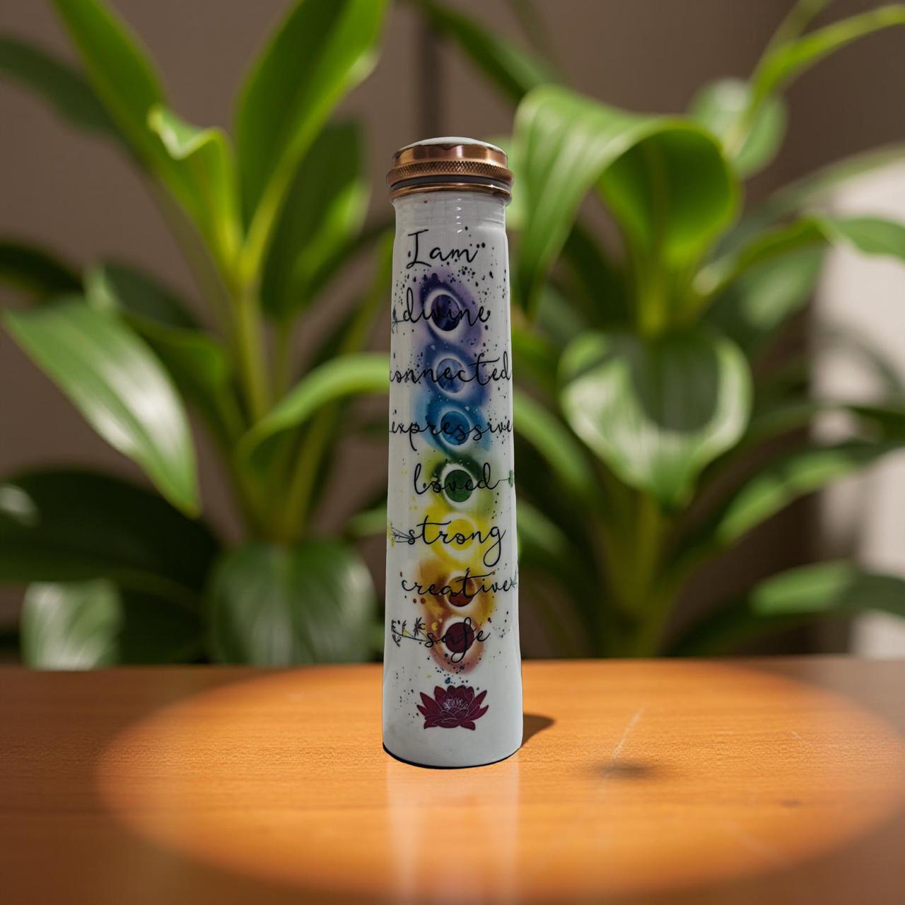 Tall copper bottle with motivational text and colorful symbols on a wooden surface with plants in the background