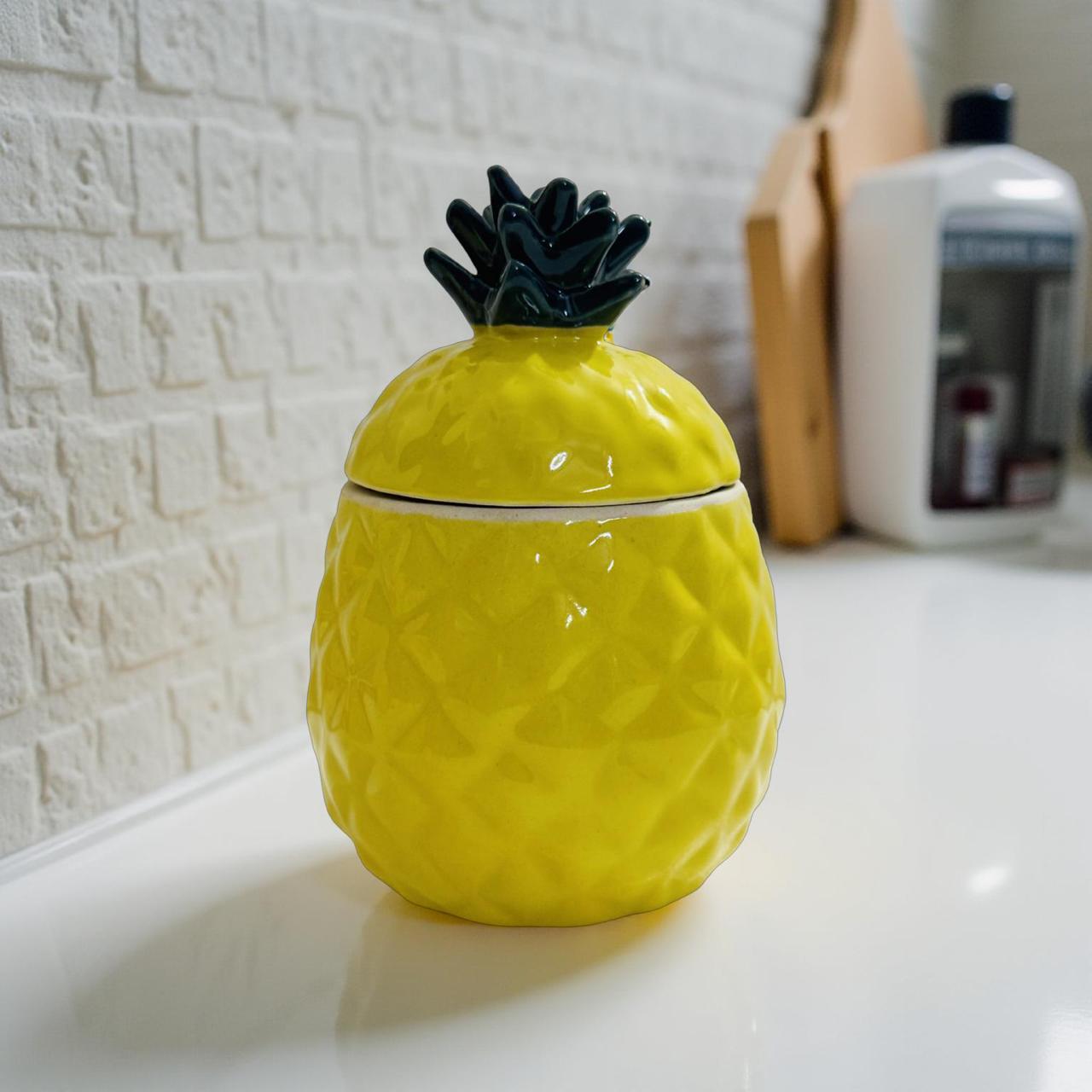 Yellow pineapple-shaped container with a black top on a white surface.
