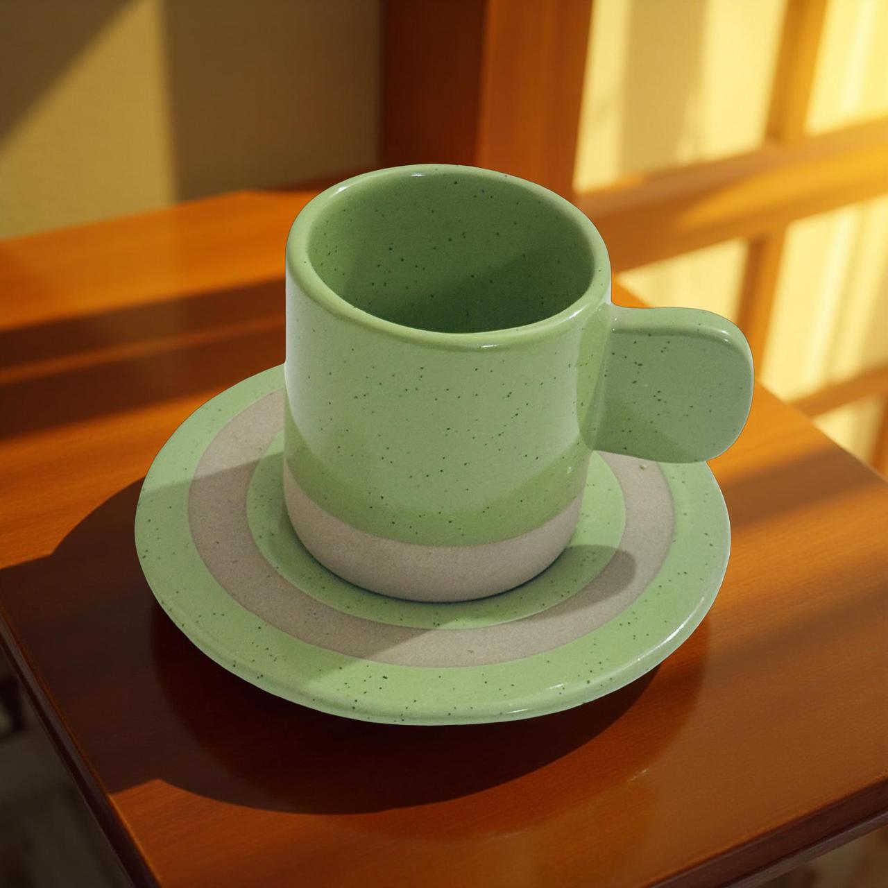 Green ceramic cup and saucer on a wooden surface with sunlight filtering through a window.
