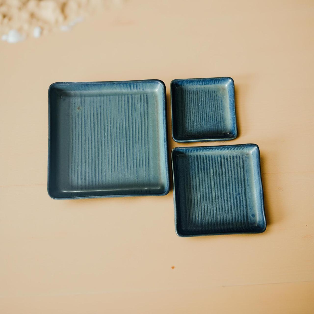 Three blue square ceramic plates on a beige background