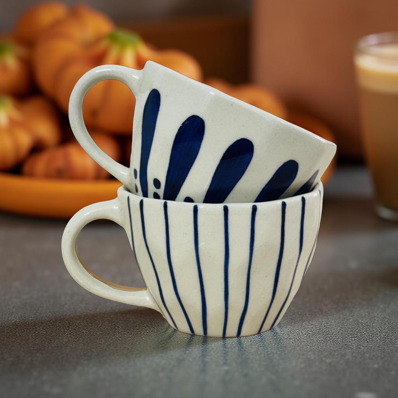 Two ceramic cups with blue patterns stacked on a table, with pumpkins in the background.