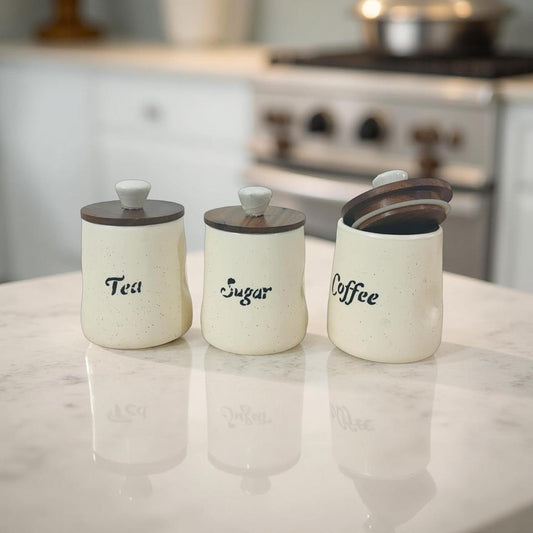 Three ceramic canisters labeled 'Tea', 'Sugar', and 'Coffee' on a kitchen counter.