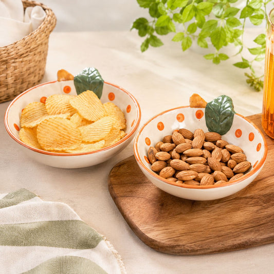 Two bowls of snacks on a wooden board with a plant in the background