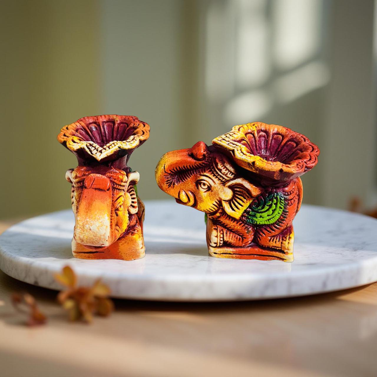 Two colorful elephant-shaped candles on a marble plate with a blurred background