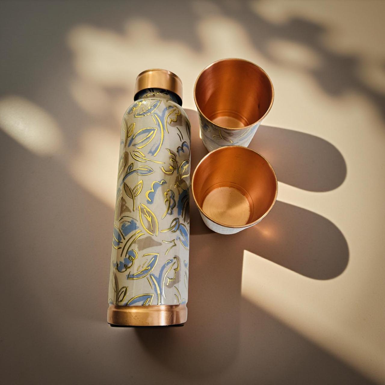 Floral-patterned water bottle with two copper cups on a textured surface