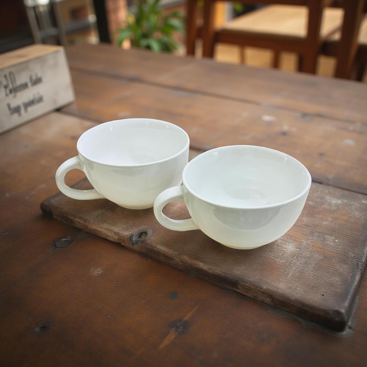 Two white ceramic cups on a wooden surface with a rustic background