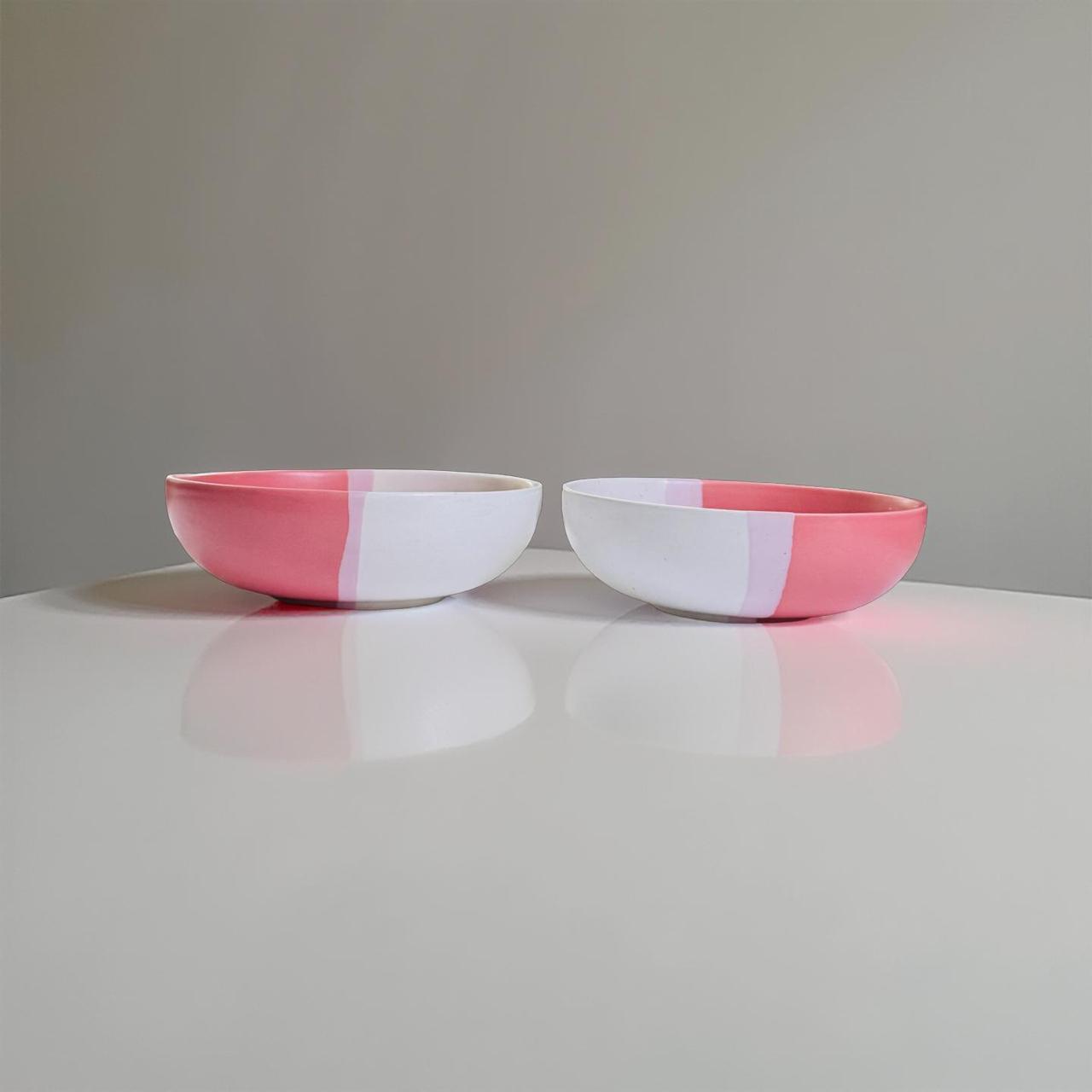 Two ceramic bowls with pink and white striped design on a reflective surface.