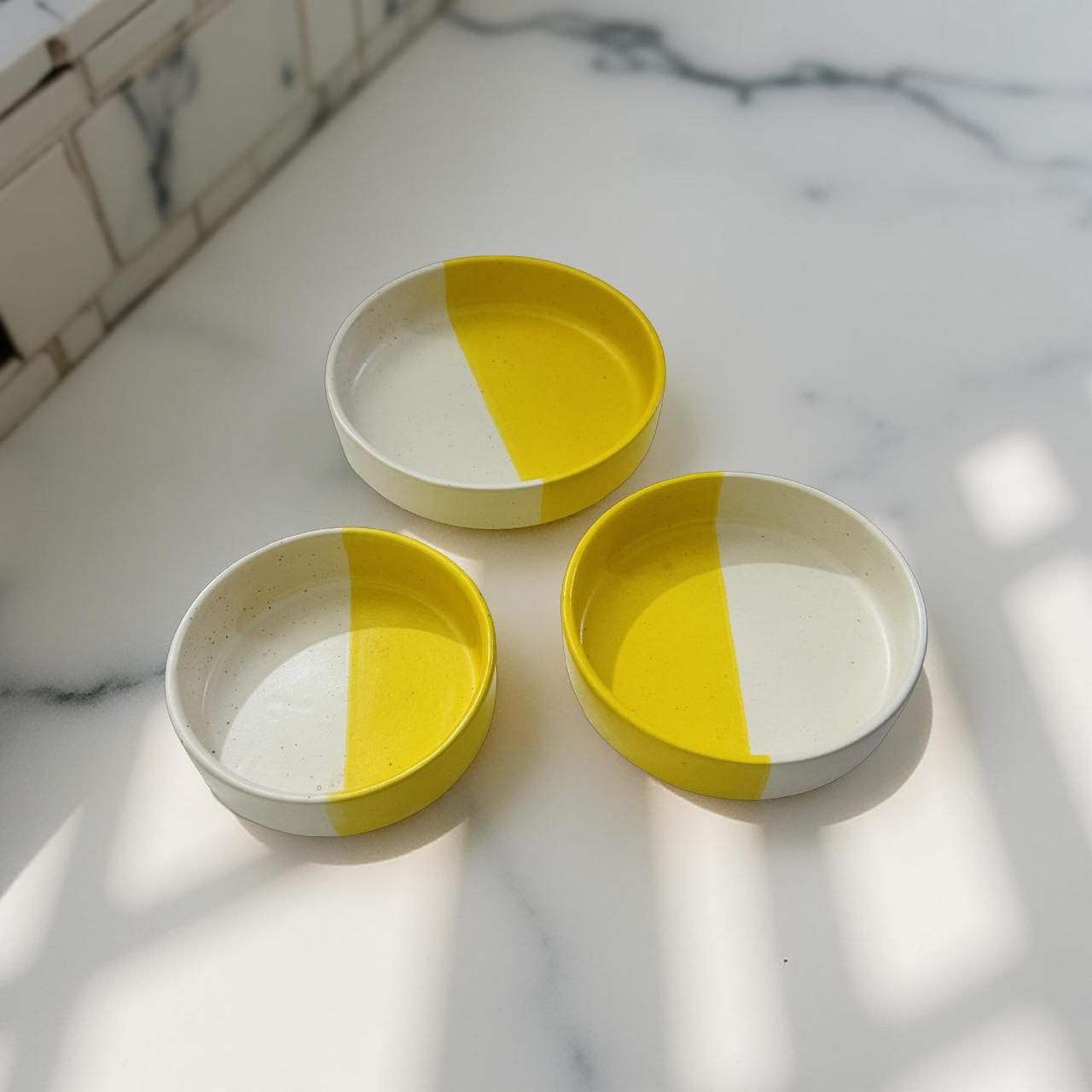 Three ceramic bowls with yellow and white design on a marble surface