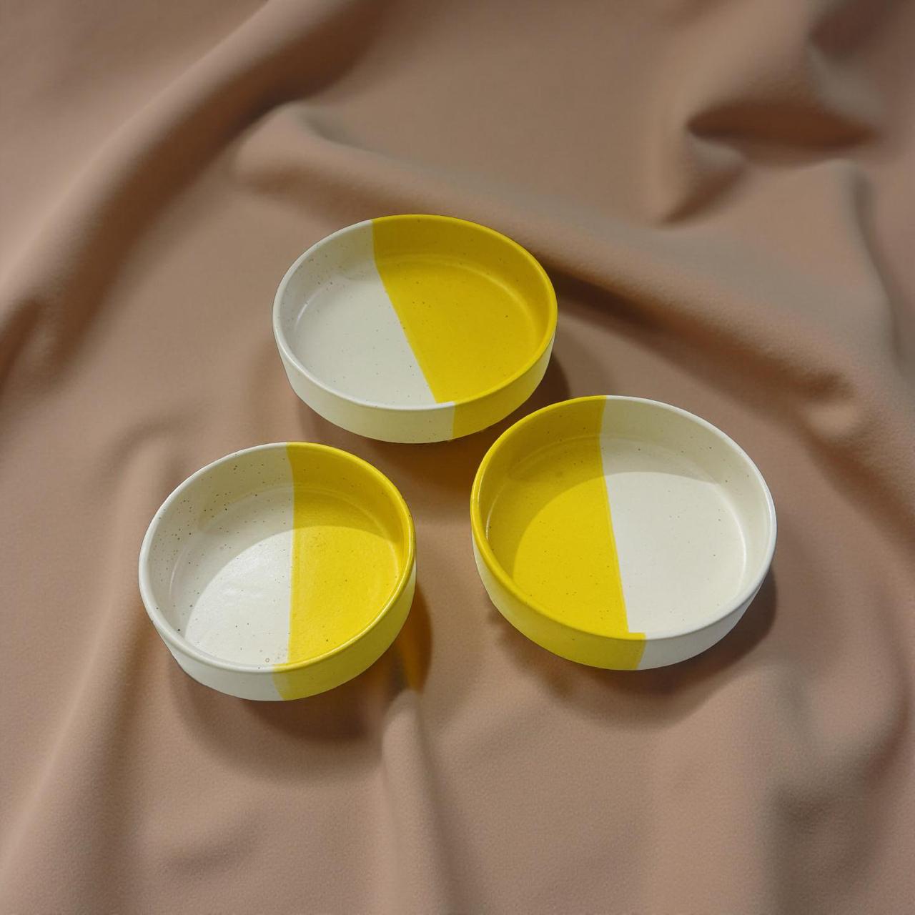 Three yellow and white ceramic dishes on a brown fabric background