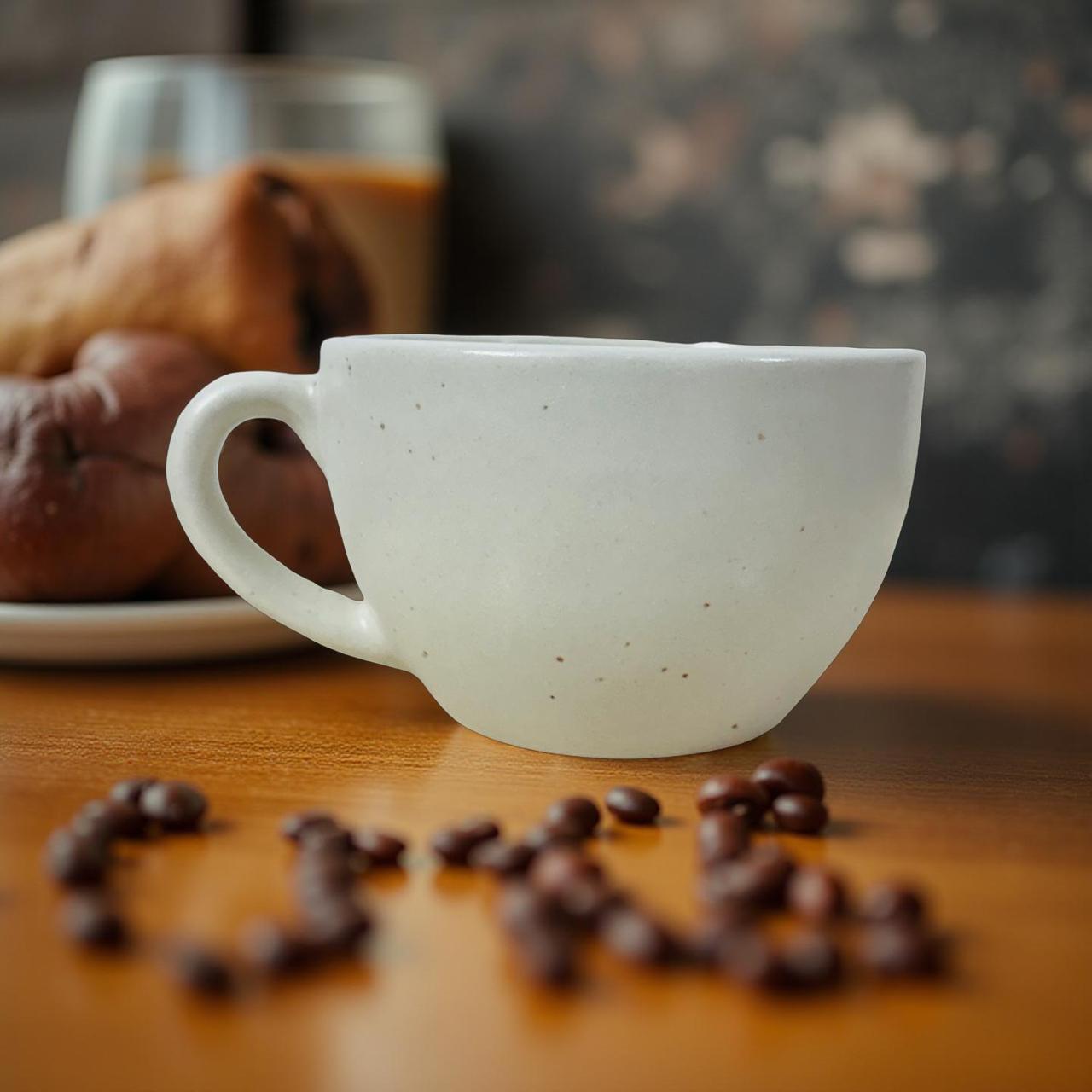 White ceramic mug on a wooden surface with coffee beans and pastries in the background