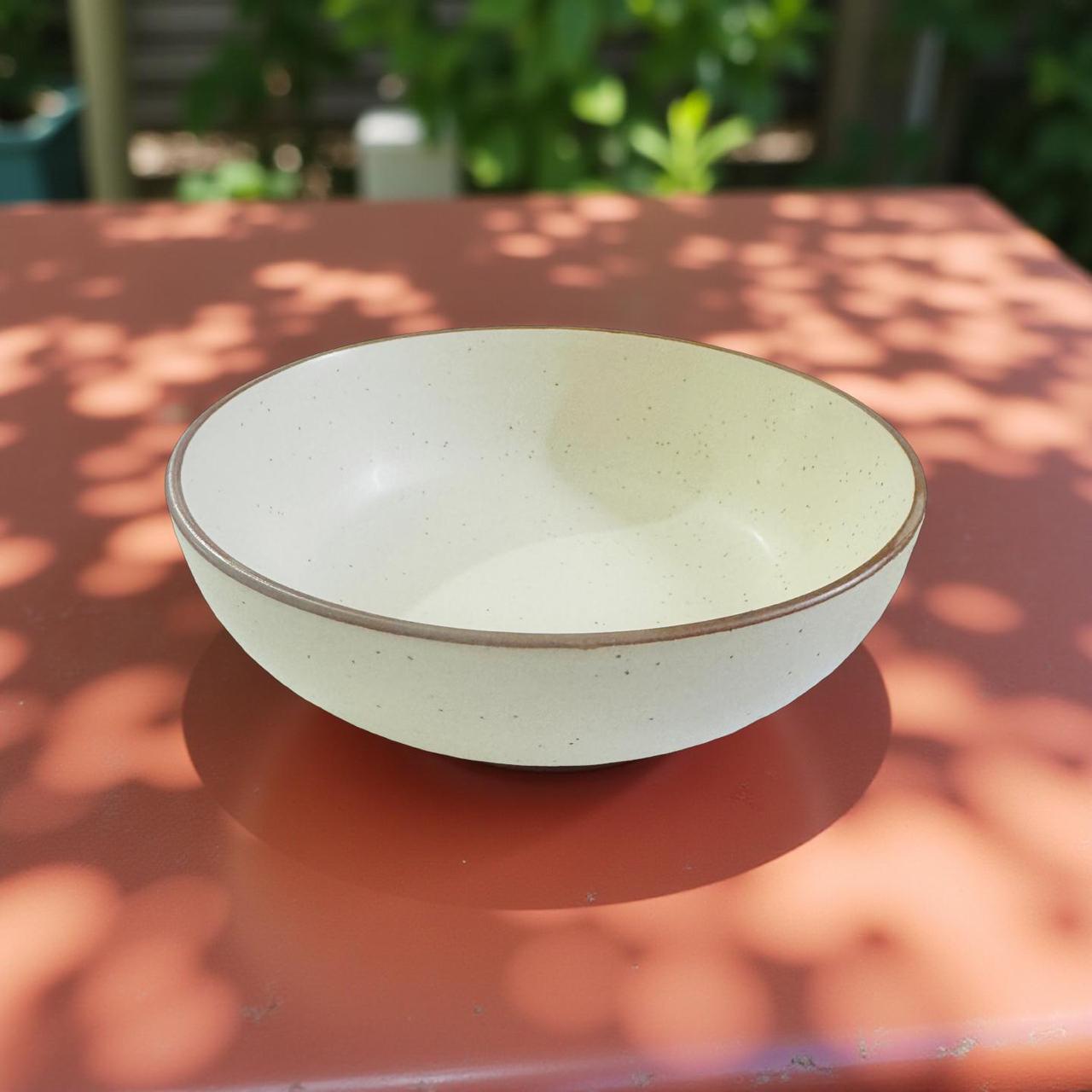 White ceramic bowl on a brown surface with blurred greenery in the background
