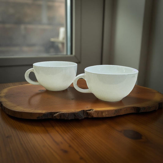 Two white ceramic cups on a wooden tray with a window in the background