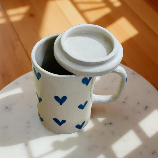 White mug with blue heart patterns and a white lid on a marble surface with wooden background