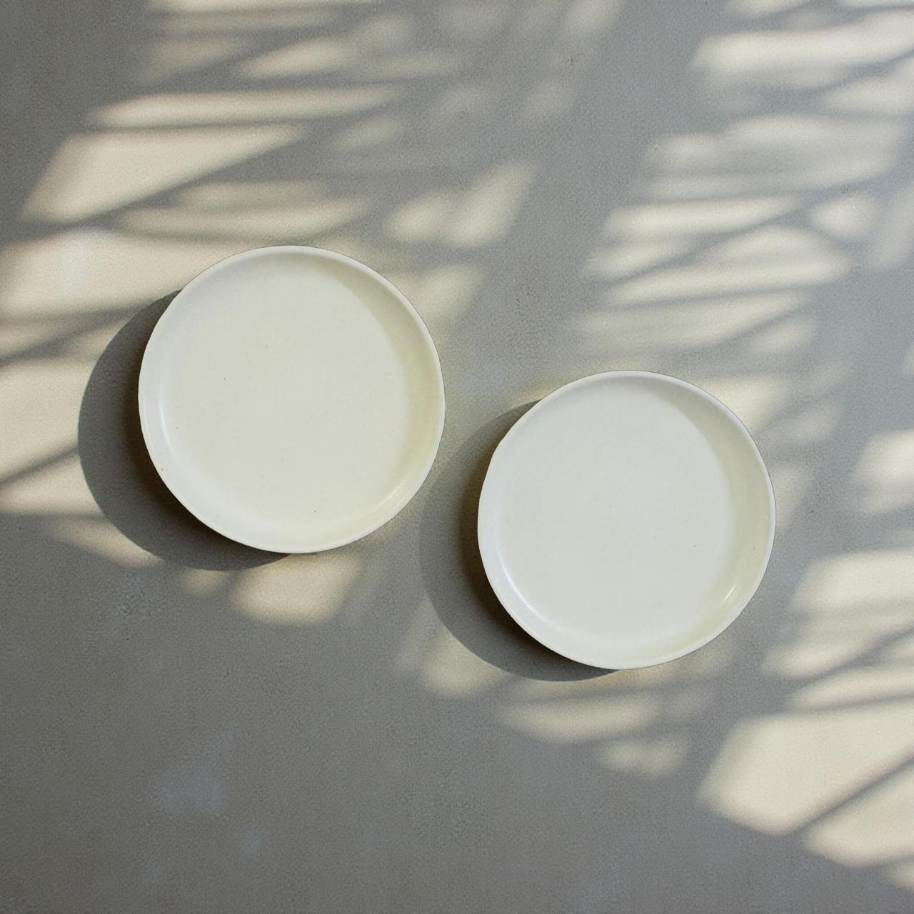 Two white ceramic plates on a gray surface with shadow patterns
