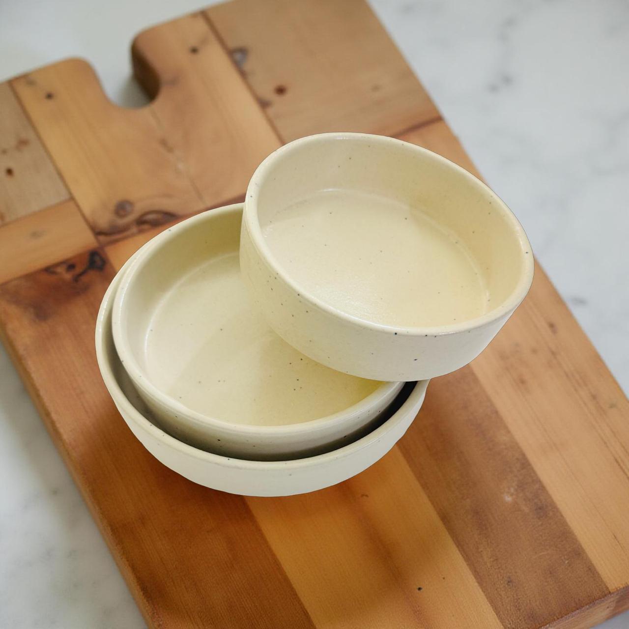 Three ceramic bowls stacked on a wooden cutting board
