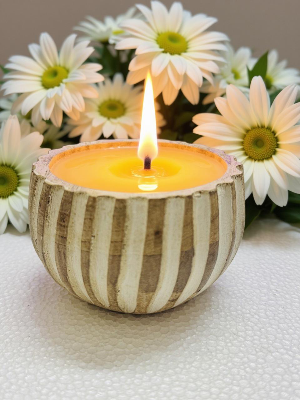 Candle in a striped container with flowers in the background