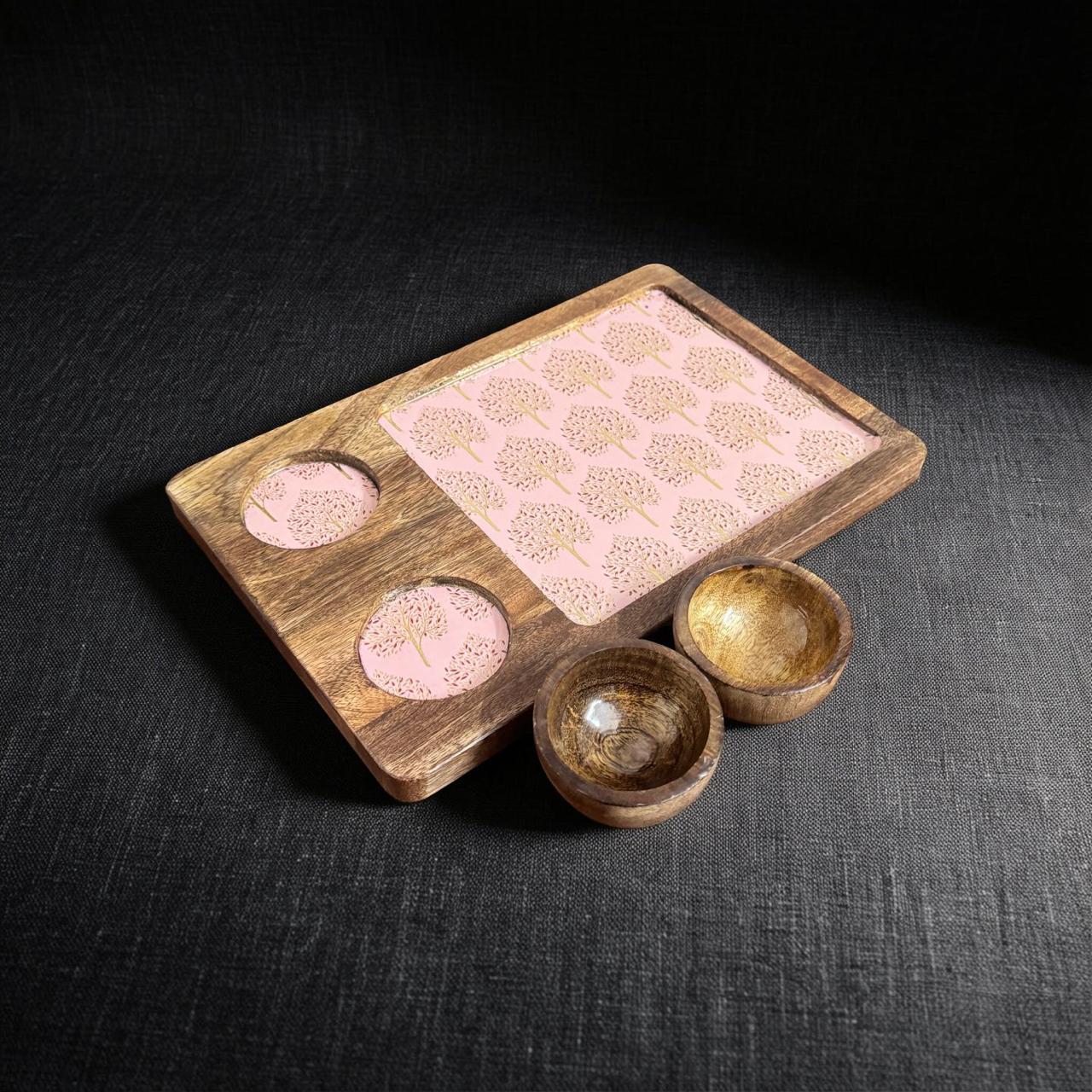 Wooden tray with pink and gold items on a dark fabric background