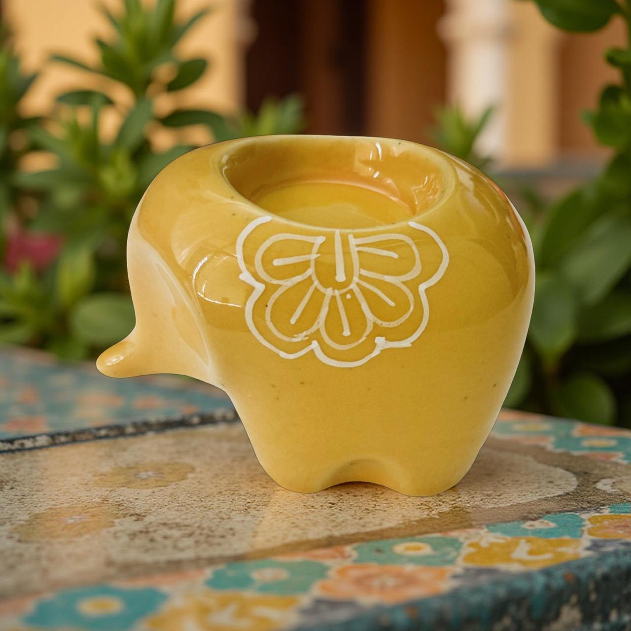 Yellow ceramic elephant planter with a floral design on a patterned surface with plants in the background
