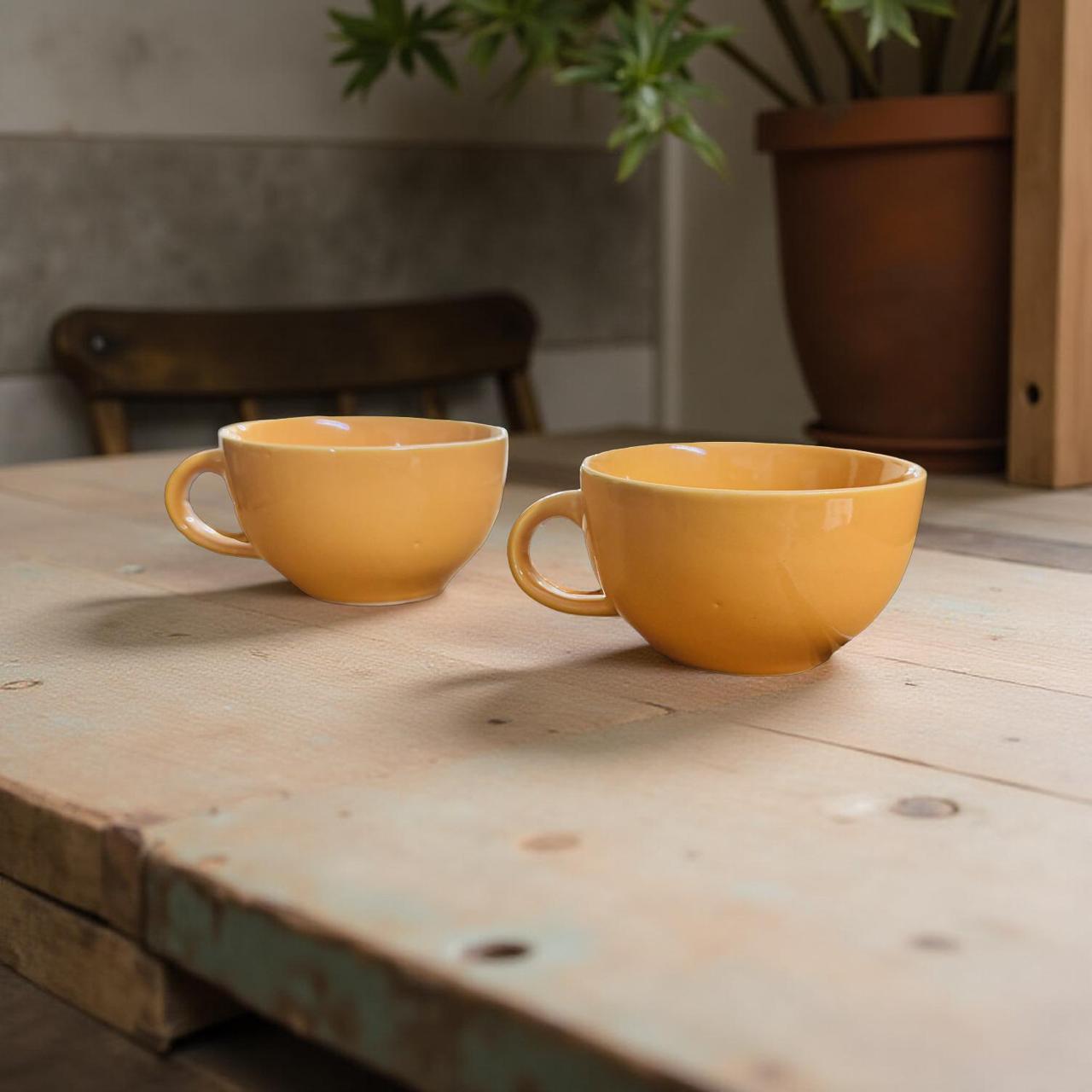 Two yellow ceramic cups on a wooden surface with a plant in the background.