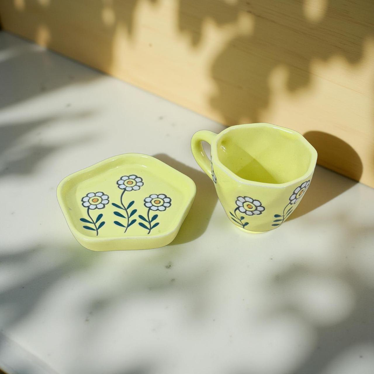 ceramic yellow daisy mug and saucer set kept on a polished surface with wooden background.